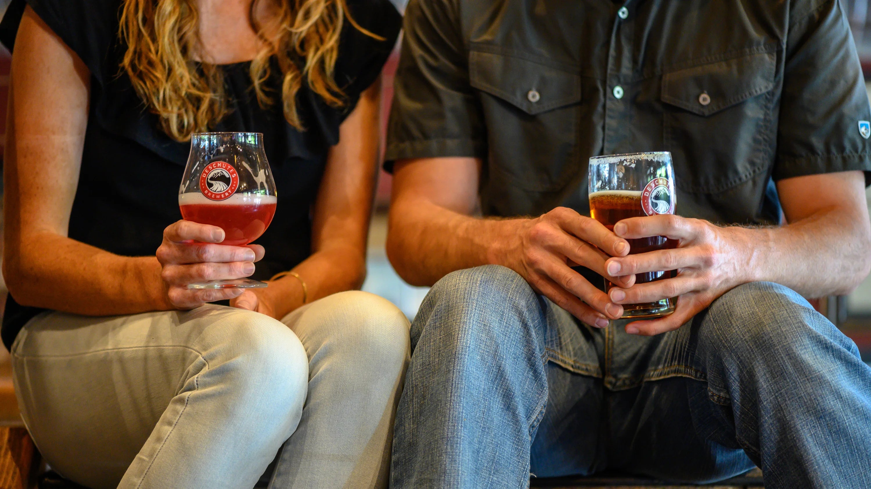 A closeup of two friends holding beers in Deschutes branded glassware.