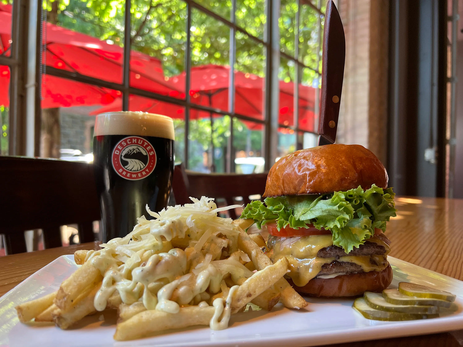 A photograph of burgers and fries with a beer on an inside table.