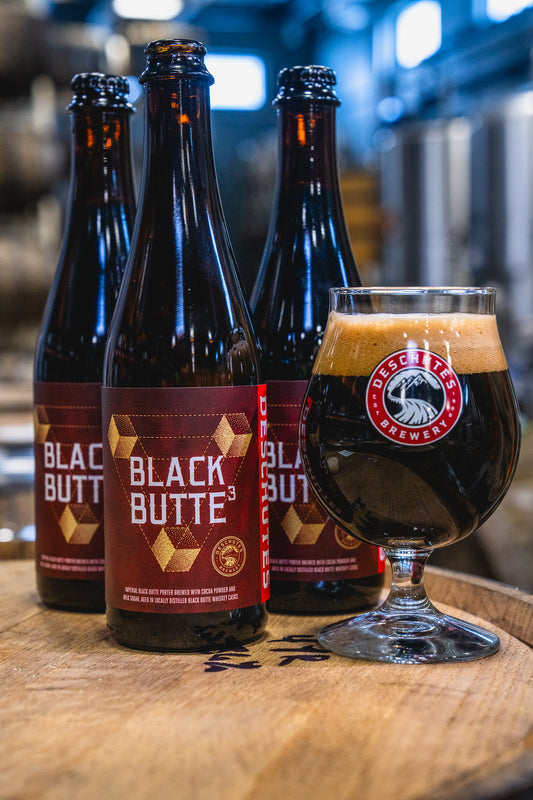 Three bottles of Black Butte cubed beer with a glass of beer on a wooden surface.