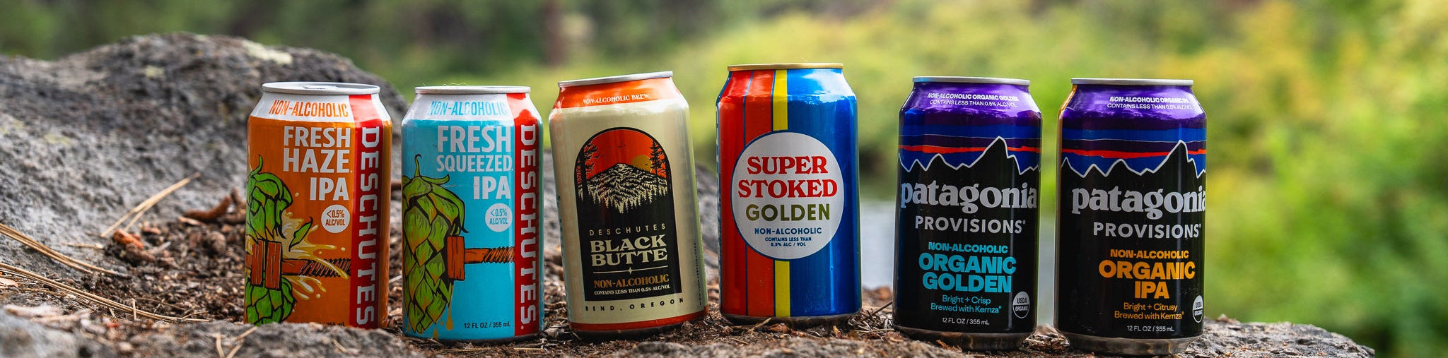 Assorted beer cans on a rock with a forest background.