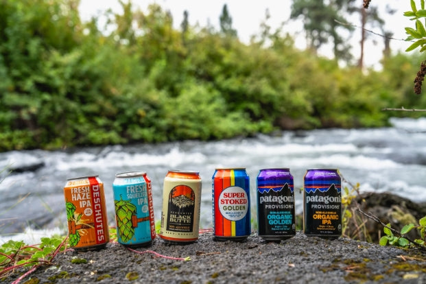 Six cans of our Non-Alcoholic beers arranged on a rock by a river