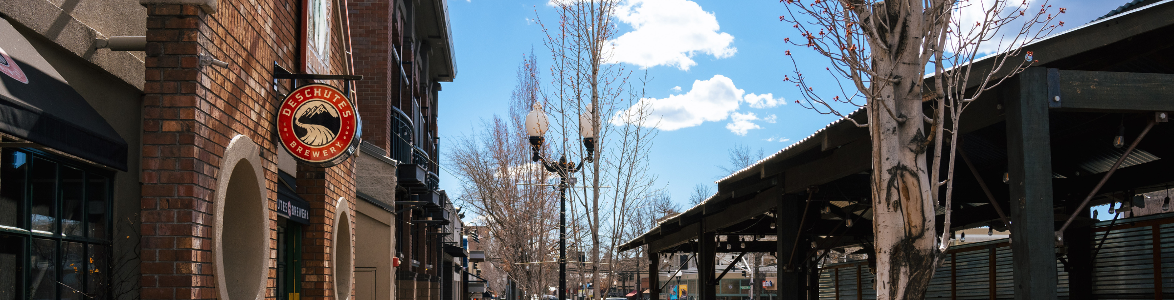 Street scene with brick building, streetlights, and cars under a blue sky with clouds.